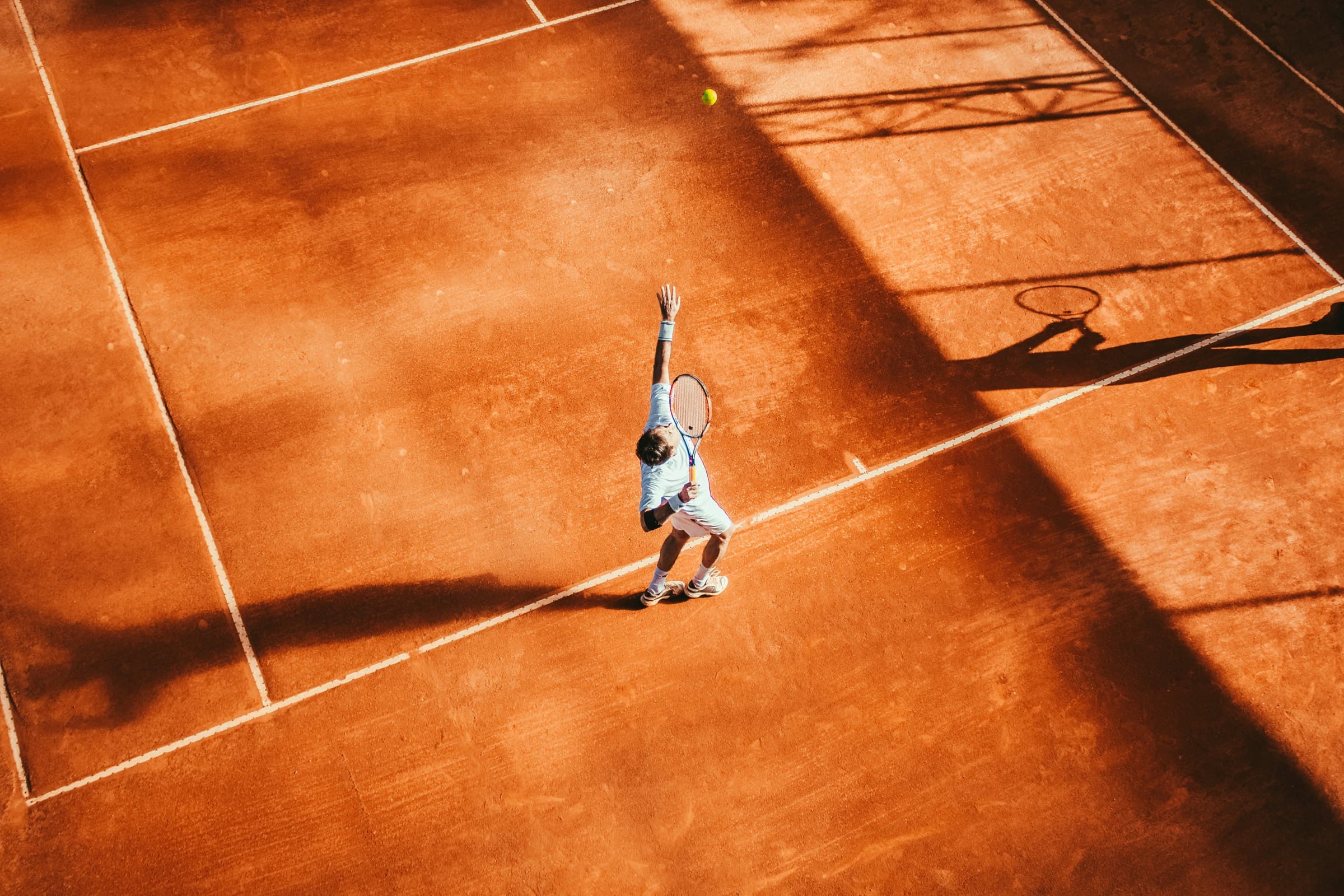 Clay tennis court at Meru Clay, a player serving in the low Arusha sun